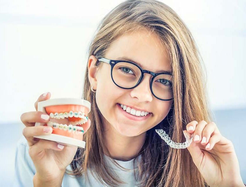 Smiling teenage girl holding a clear aligner