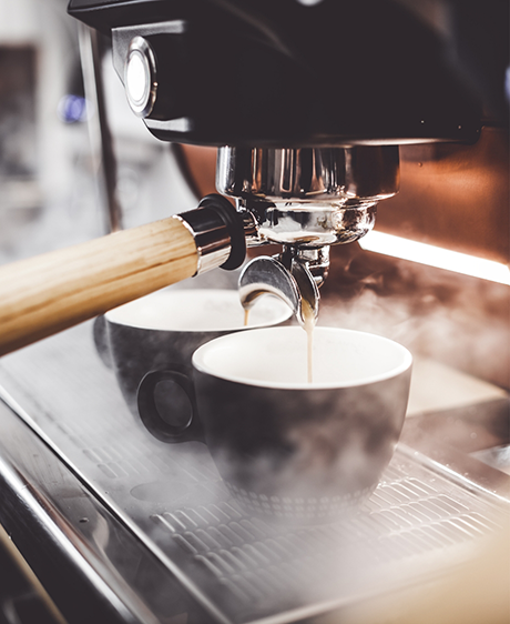 Coffee maker pouring coffee into two black mugs