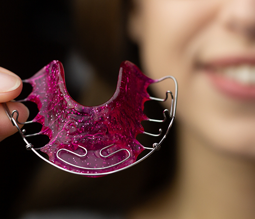 Smiling person holding a sparkly pink retainer