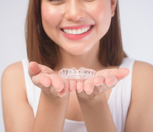 Smiling woman holding two clear aligners in her open palms