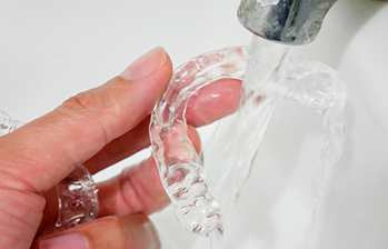 Person cleaning a clear aligner in a sink