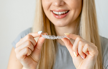 Blonde woman holding an aligner near her smile