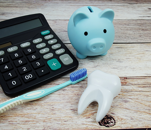 Piggy bank next to a calculator, a tube of toothpaste, and a model of a tooth