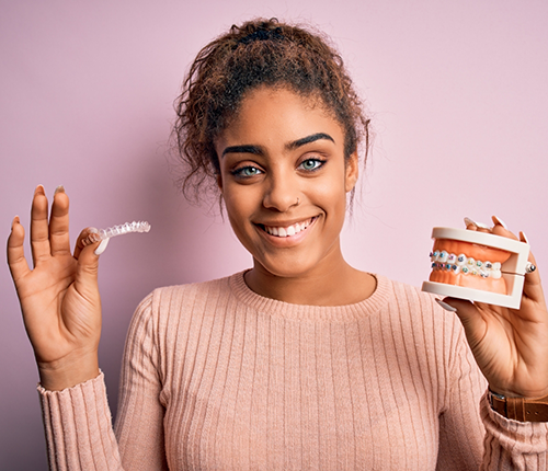 Smiling woman holding clear aligners in one hand and a model of the teeth with bracs in the other
