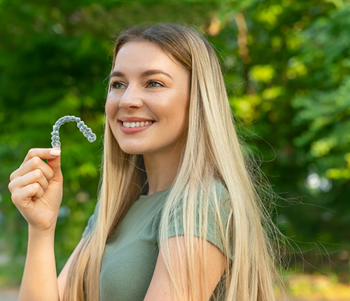 Smiling blonde woman holding a clear aligner